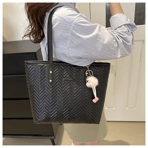 Close-up of black quilted tote bag with V-shaped stitching and pink plush pendant