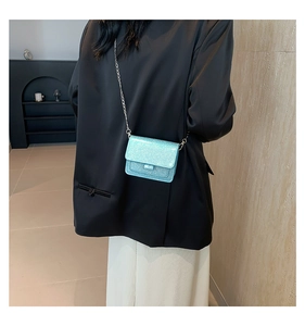 Gros plan d'un mini sac bleu à paillettes avec chaîne argentée sur un blazer noir