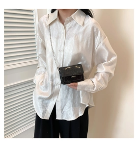Détail de la texture d'une chemise plissée blanche avec un petit sac à chaîne à paillettes