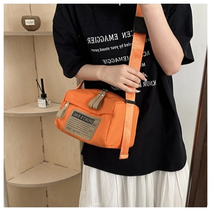 Gros plan du sac cylindre orange en tissu Oxford avec large bandoulière porté par mannequin