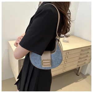 Detail view of denim and beige leather crescent shoulder bag with golden metallic buckle