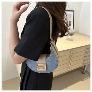 Detail of blue denim crescent bag with beige leather trim and gold square buckle