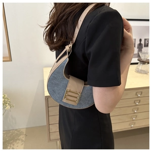 Blue denim half-moon underarm bag with beige leather trim and gold buckle detail