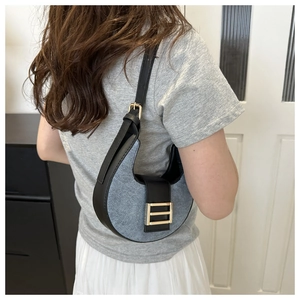 Detail of blue denim and black leather shoulder bag with golden hardware on a model