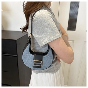 Detail of denim and black leather hobo bag with gold buckle shown on shoulder