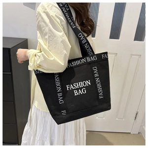 Close-up of black canvas tote bag with white FASHION BAG lettering worn by a model