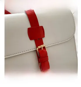 Détail du sac en similicuir blanc texturé avec bandoulière rouge et boucle dorée