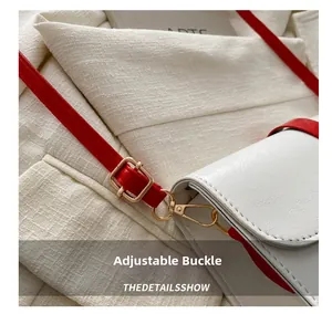 Détail de la bandoulière rouge réglable avec boucles dorées sur sac en cuir blanc