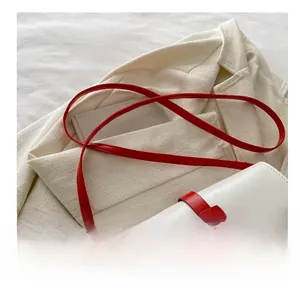 Détail du sac bandoulière blanc avec bandoulière rouge vif et boucle métallique dorée