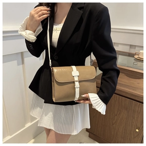 Détail du sac bandoulière kaki sur un blazer noir et une jupe plissée blanche