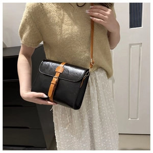 Détail d'un sac à bandoulière rétro en noir avec sangle marron et boucle dorée élégante