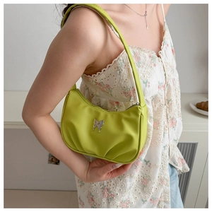 Détail du sac porté épaule croissant vert citron avec papillon argenté sur robe blanche
