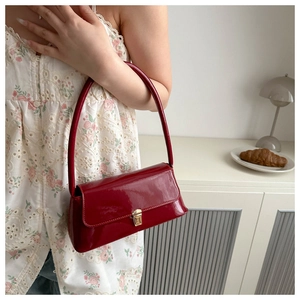Détail du sac sous le bras en cuir verni rouge avec boucle dorée et fini brillant