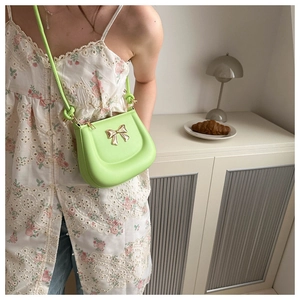 Detail of neon green handbag with gold bow buckle and knotted strap on minimalist desk