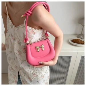 Close-up of bright pink shoulder bag featuring a decorative gold bow and knotted handle