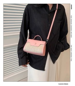 Detail of pink leather and beige woven straw handbag worn by model against window