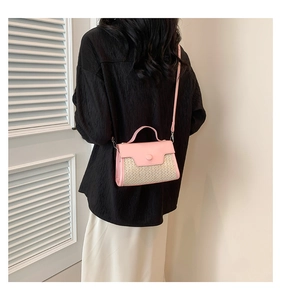 Detail of pink leather and woven straw crossbody bag shown on a model in a minimalist setting