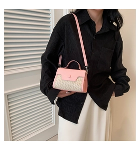 Detail of pink and beige woven patchwork handbag held by a model in a black shirt