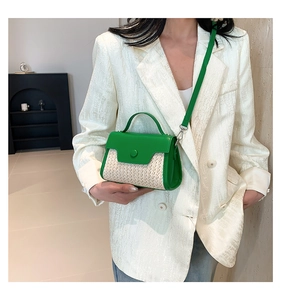 Detail view of a mini green leather and woven straw crossbody bag held by a model