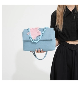 Detail of light blue denim crossbody bag featuring a pink star patch and plastic chain