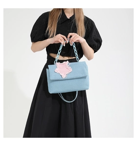 Detail of light blue denim handbag with pink frayed star patch and acrylic chain handle
