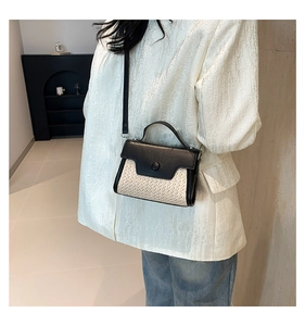 Detail view of woven straw shoulder bag with black leather flap and handle accents