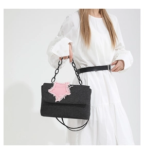 Detail of dark denim shoulder bag with pink frayed star patch and chunky chain strap