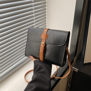 Sac bandoulière carré chic noir et marron avec boucle dorée près d'une fenêtre