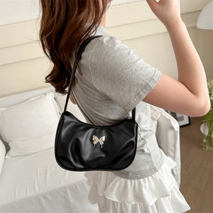 Sac hobo noir minimaliste avec papillon argenté porté à l'épaule par un mannequin