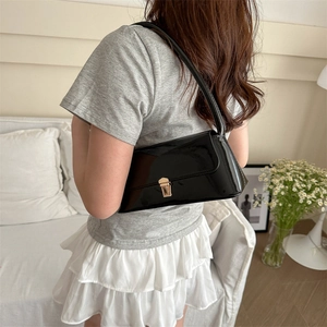 Sac baguette rétro en cuir verni noir avec boucle dorée porté sur l'épaule
