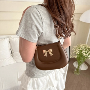 Deep brown shoulder bag with gold bow detail worn by a model in a cozy indoor setting