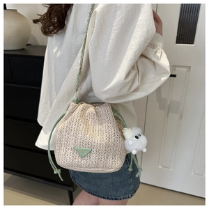Detail der gewebten Stroh-Eimertasche mit mintgrünem Kettengurt und Plüschanhänger
