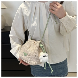 Detail der gewebten Stroh-Eimertasche mit grünem Besatz und Plüschmonster-Anhänger