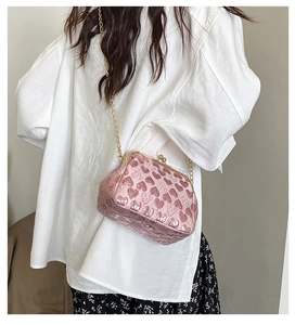 Detailed view of pink heart-embossed evening bag with elegant gold chain strap worn by model