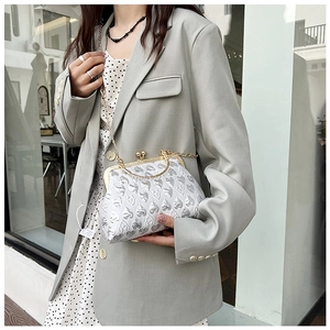 Detail of silver jacquard shell bag with heart pattern and gold chain strap on a model
