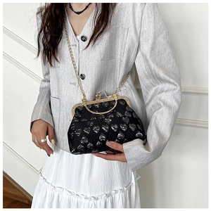 Detail of a retro black shell bag with silver heart patterns and gold chain strap