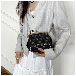 Detail of a black crossbody bag with heart pattern and vintage gold clasp on a model