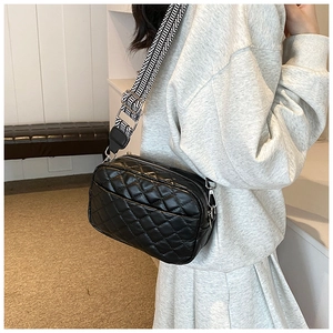 Detail of black quilted crossbody bag with stylish black and white wave pattern strap
