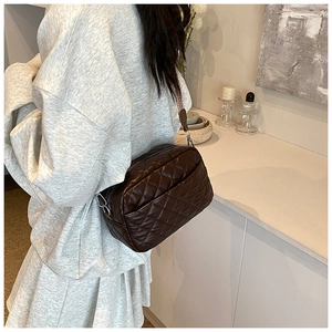 Detail of a dark brown quilted crossbody bag with adjustable strap worn by a model
