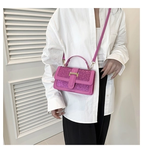 Detail of pink glitter crossbody bag with gold T-clasp and leather handle held by a model