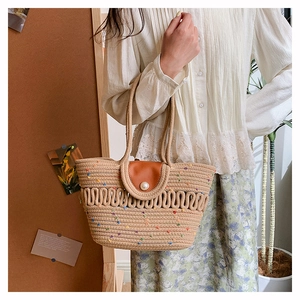 Detail of woven straw bucket bag with pearl closure and brown leather flap and handle