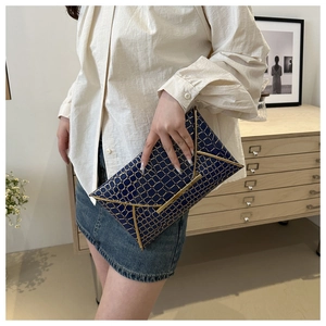 Detail der dunkelblauen Umschlag-Clutch mit goldenem geometrischem Muster und Metallleiste
