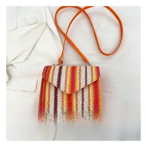 Detail of woven crossbody bag with vertical color stripes and orange leather shoulder strap