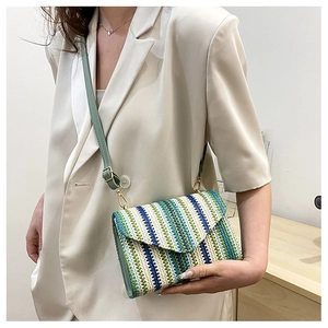 Detail of woven straw crossbody bag showing green leather strap and gold metal clasp