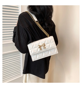 Detail of white quilted crossbody bag featuring a gold bow clasp and chain strap
