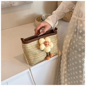 Dettaglio borsa in paglia intrecciata beige con margherita gialla e catena dorata