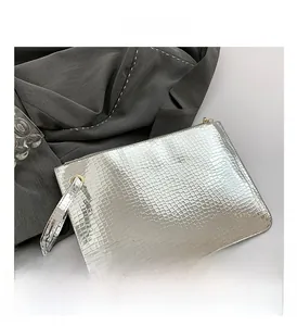 Detail view of a silver crocodile pattern clutch bag with glossy metallic finish and wrist strap