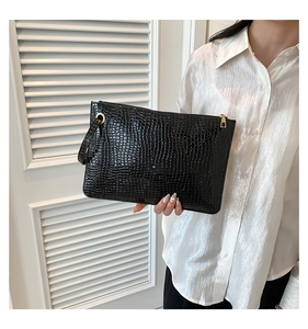 Close-up of black crocodile pattern faux leather clutch bag with golden zipper detail