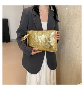 Close-up of golden metallic envelope clutch with embossed crocodile skin texture and strap