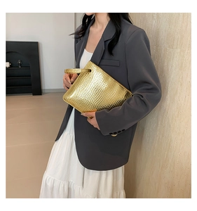 Detail of a metallic gold clutch with crocodile pattern texture held by a model